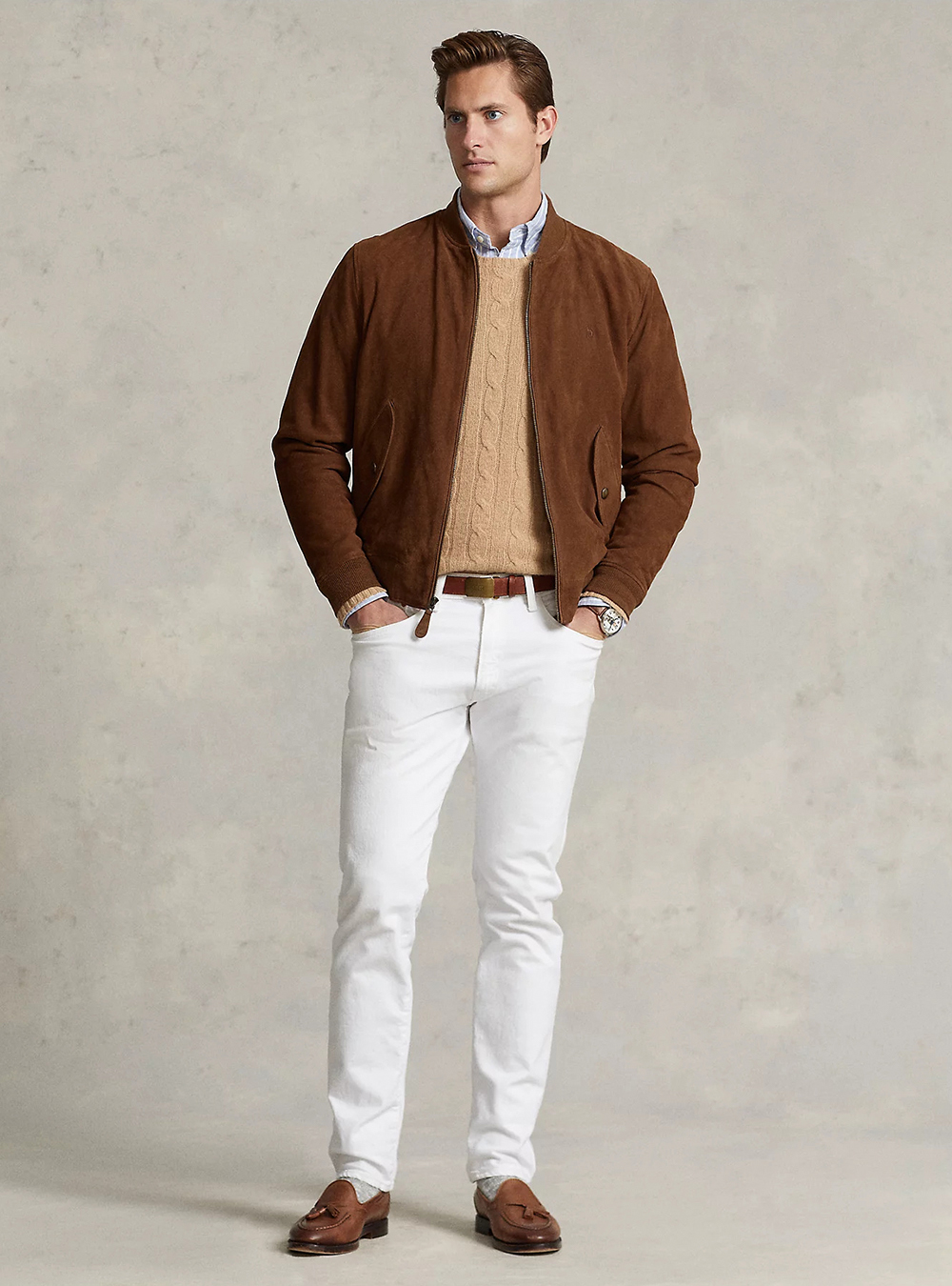 Brown suede bomber jacket, blue striped shirt, tan cardigan, white jeans, and brown loafers