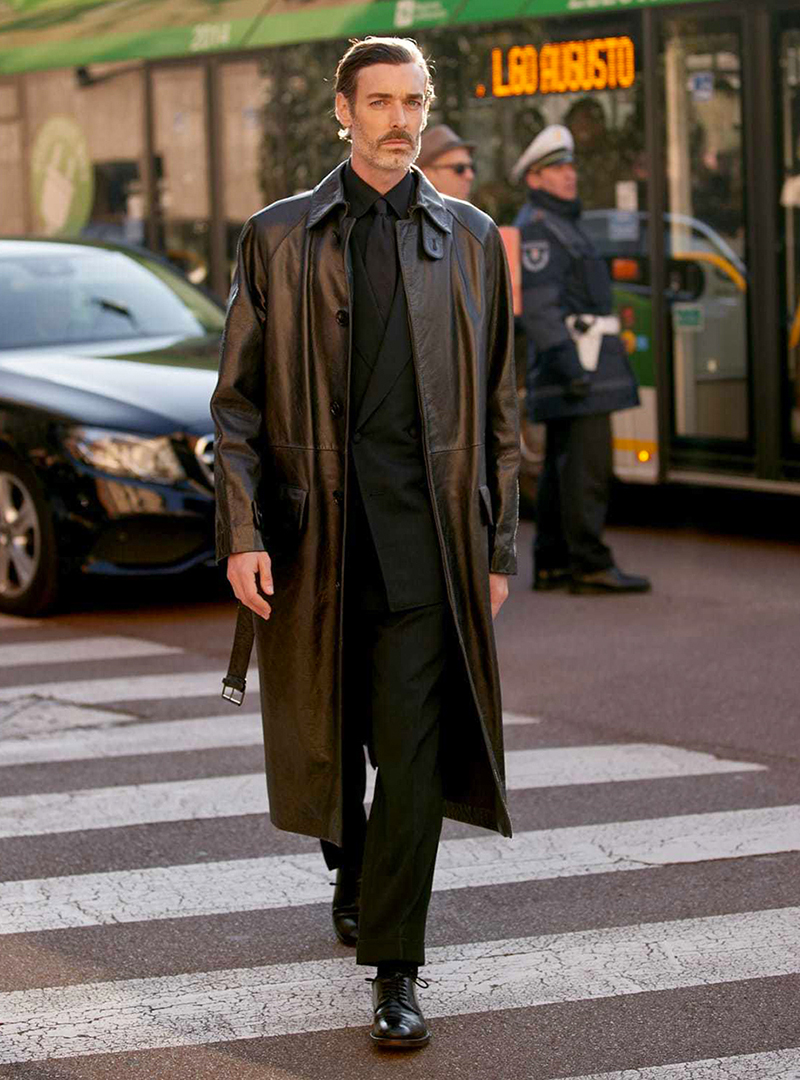 Dark brown leather overcoat, black suit, black dress shirt, dark brown tie and black leather derby shoes