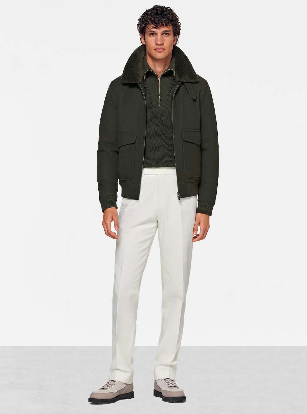 dark green bomber jacket with a half-zip sweater and off-white trousers