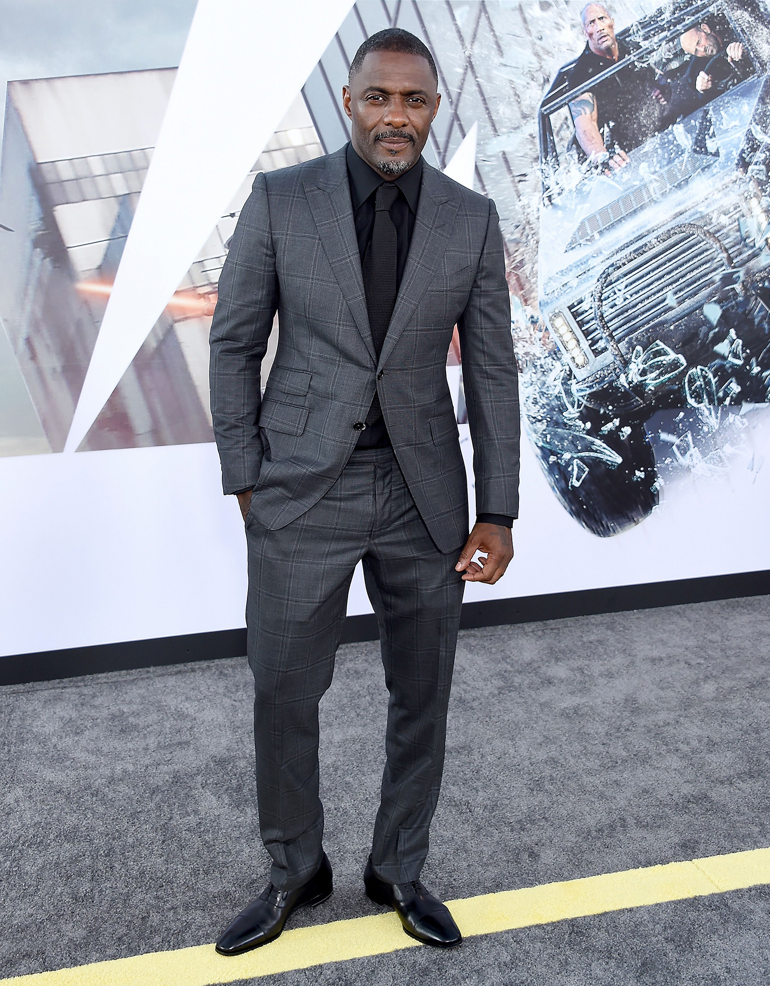 Elba wears a grey plaid suit with a black shirt