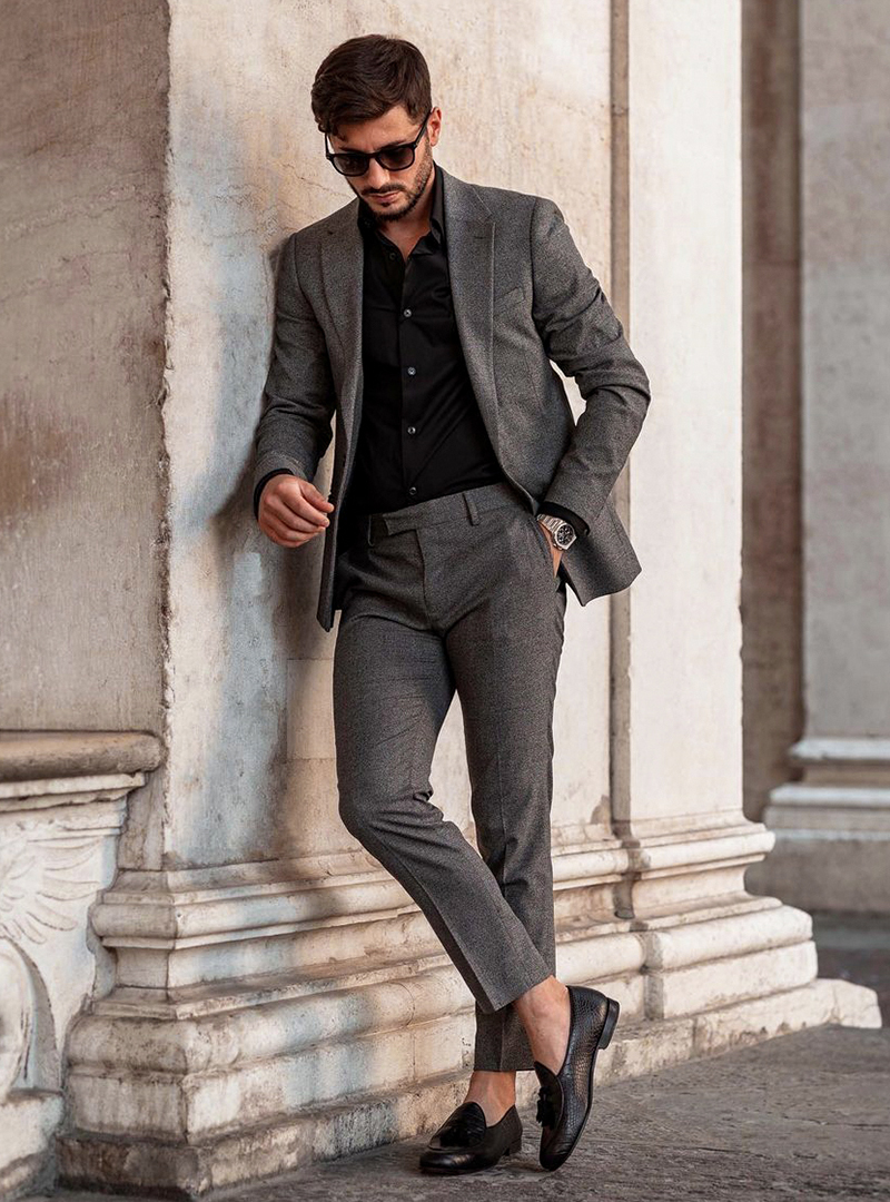 grey suit, black dress shirt, and black tassel loafers