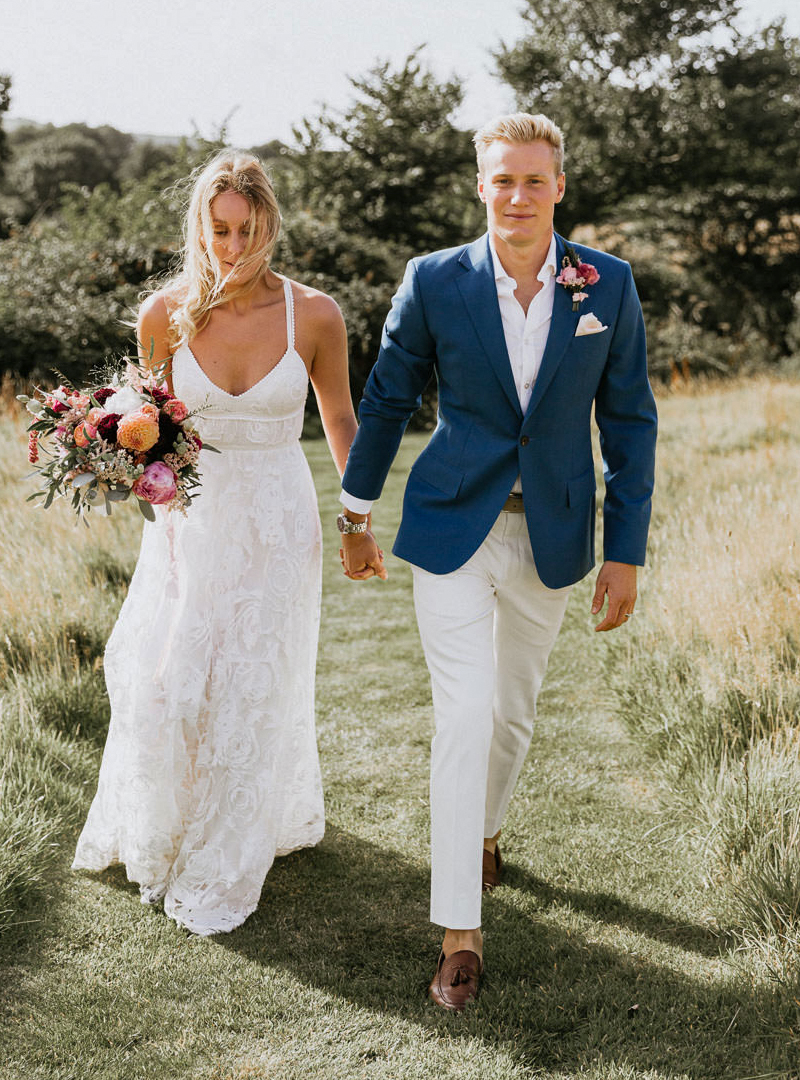 groom wears a blue jacket with a white shirt, white chino pants, and brown loafers