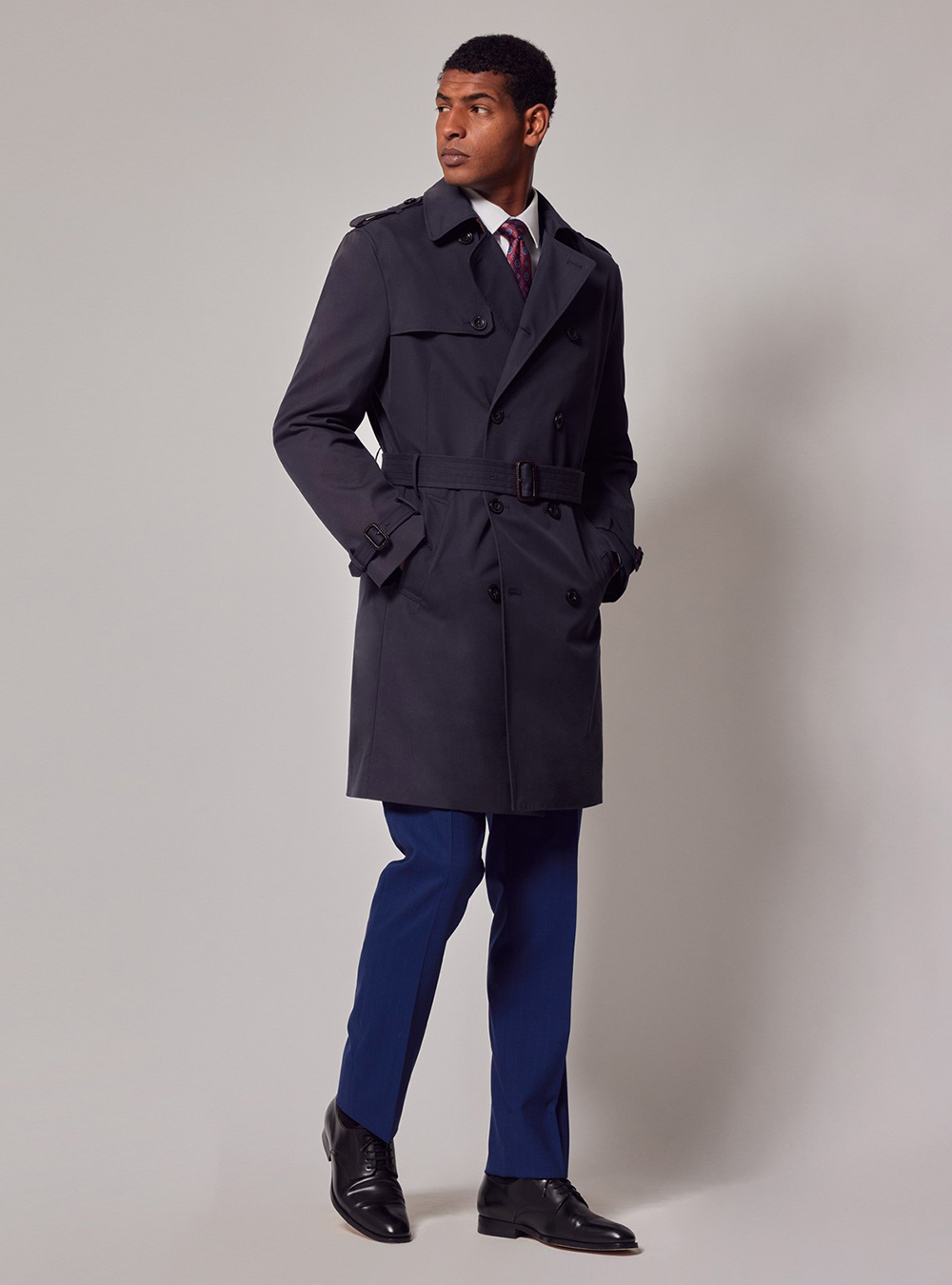 navy trench coat, white shirt, burgundy tie, blue pants, and black derby shoes