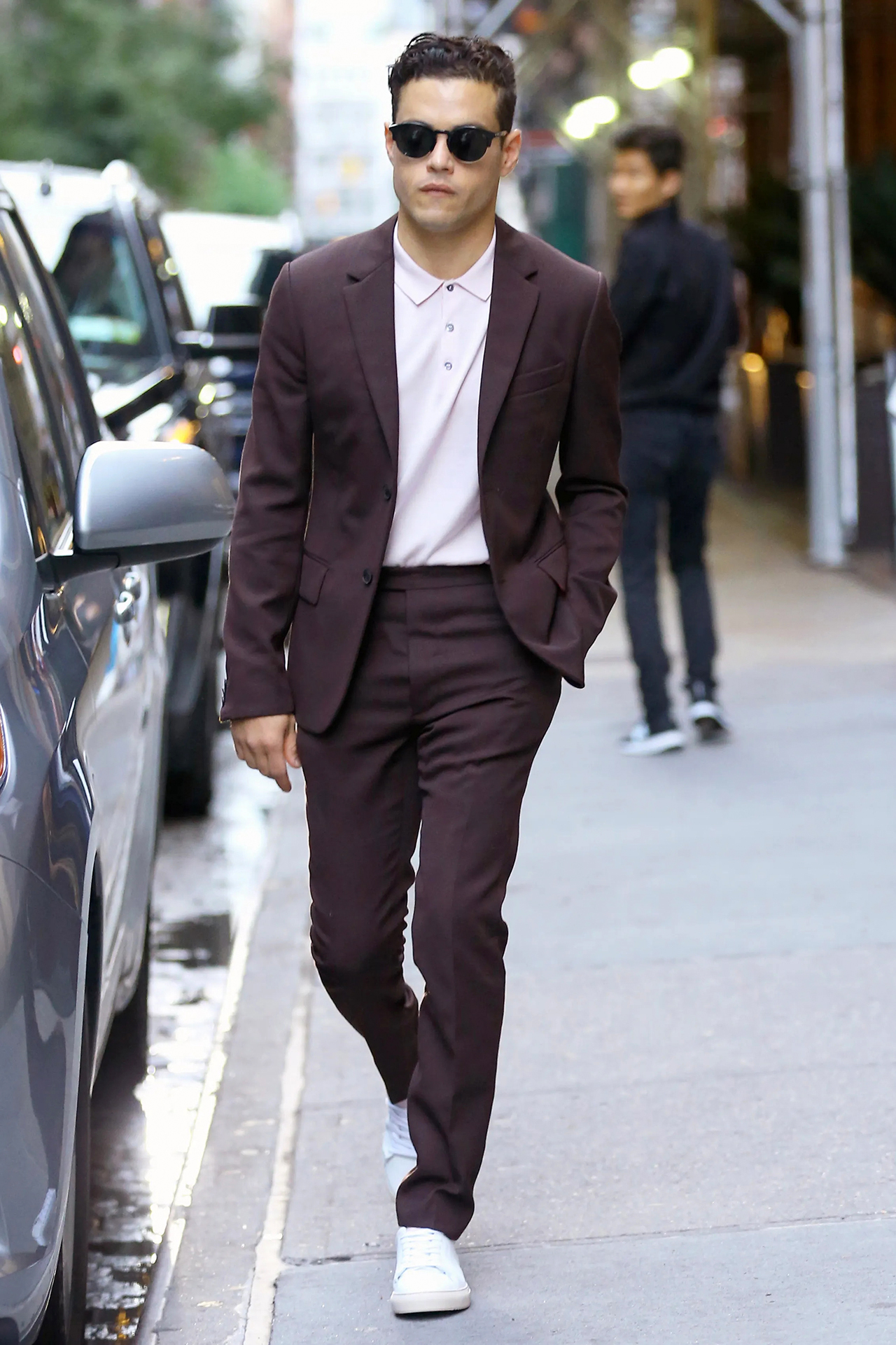Rami Malek wears a burgundy suit with a light pink polo shirt and white sneakers