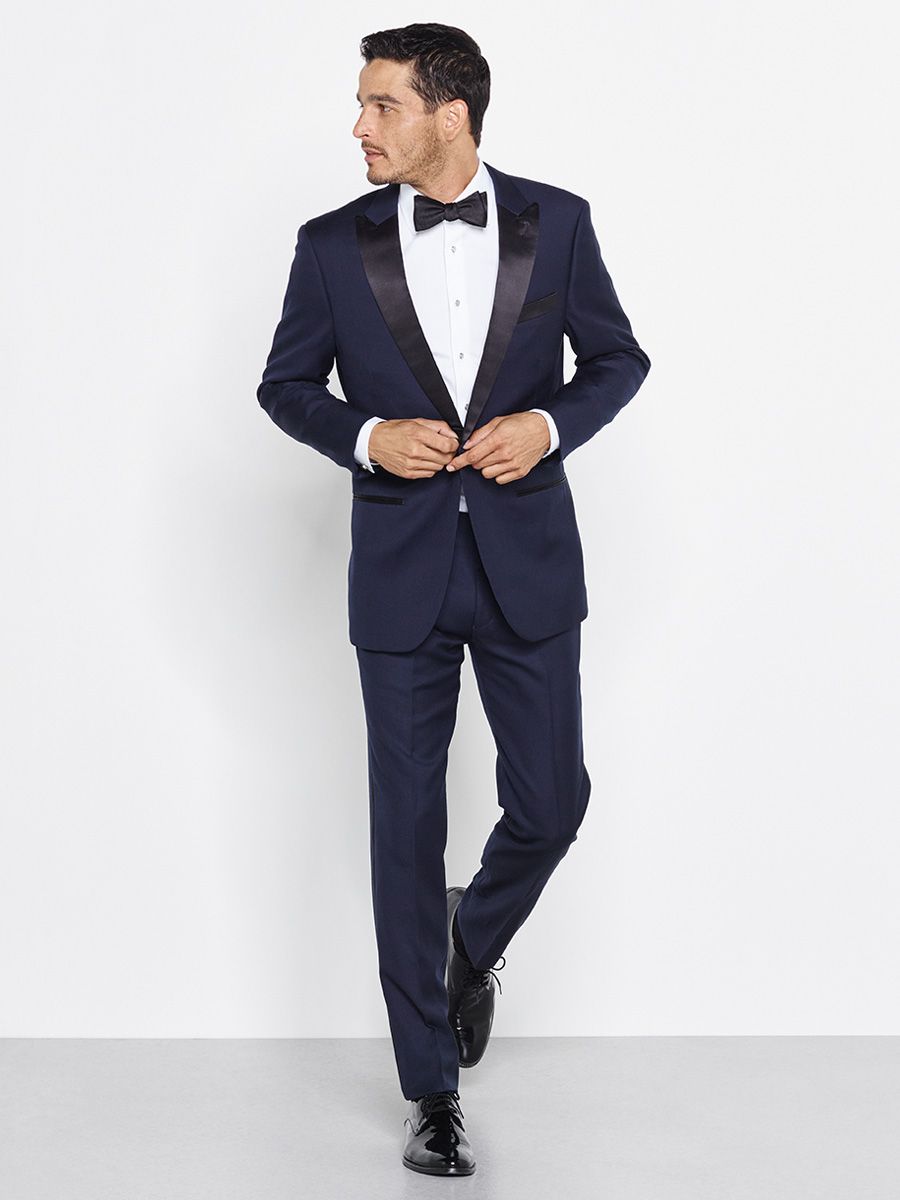 wearing a navy tuxedo, white shirt, and black Oxford shoes for a wedding